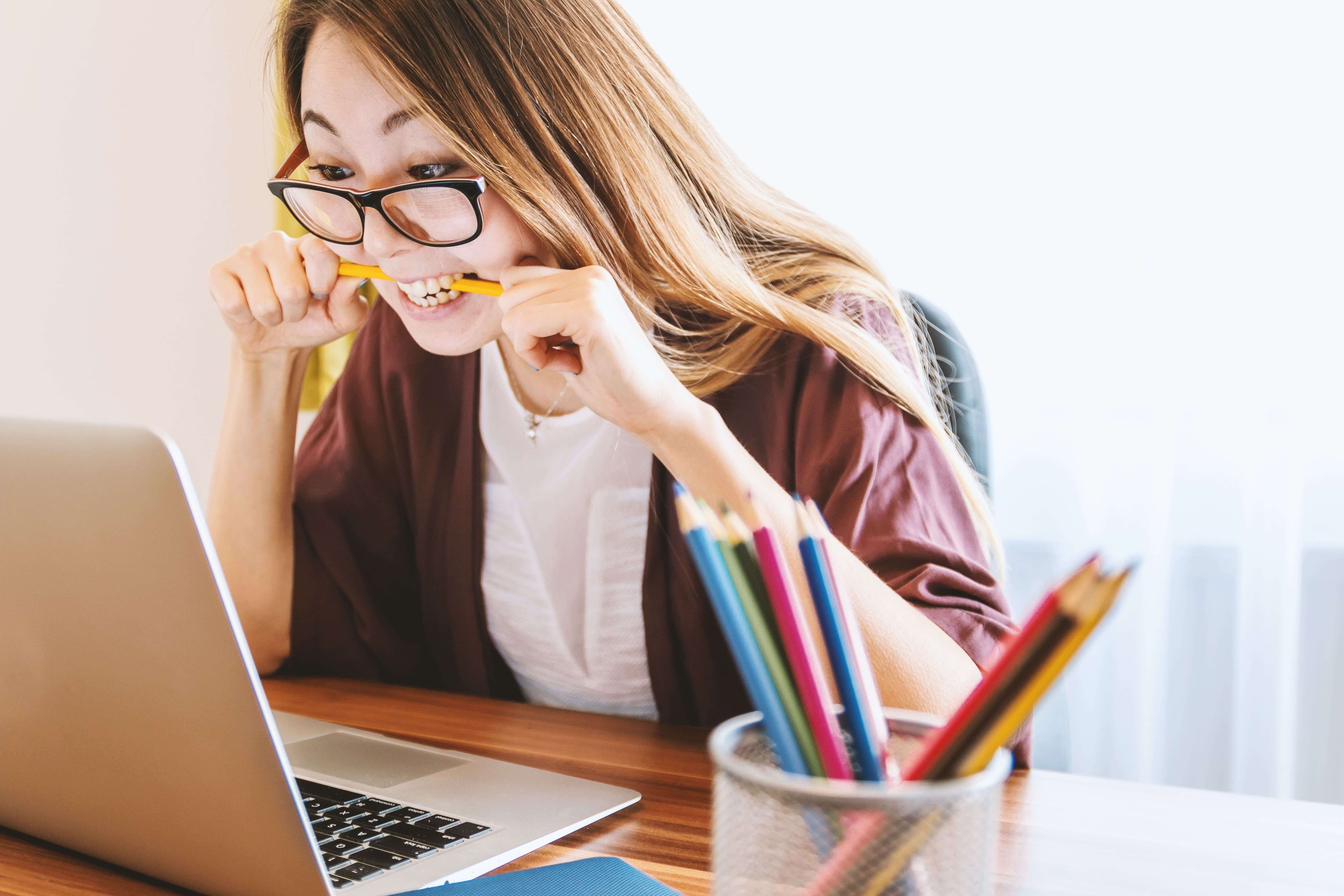 A woman biting her pencil out of frustration, in front of laptop