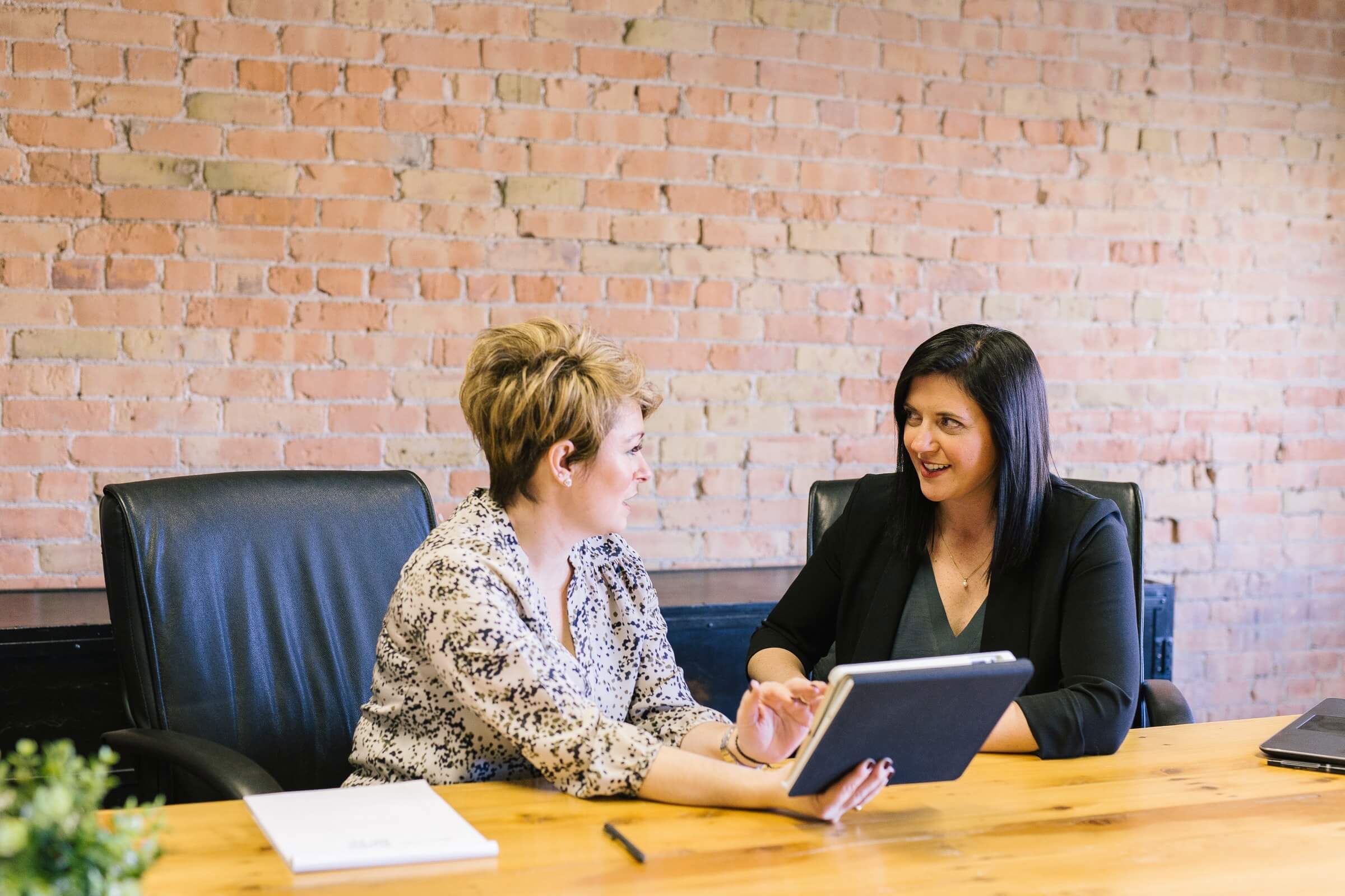 Two female colleagues discussing something at a boardroom table with a tablet