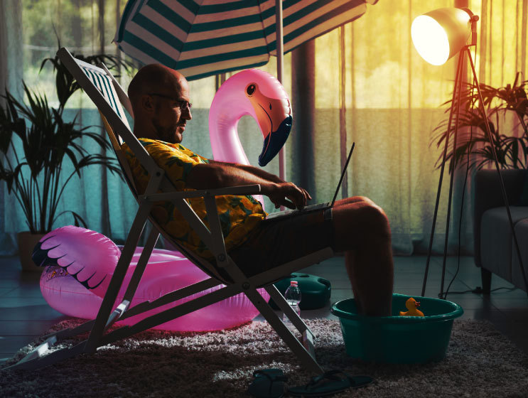 Man spending summer vacations at home alone, he is sitting on the deckchair in the living room and working with a laptop.