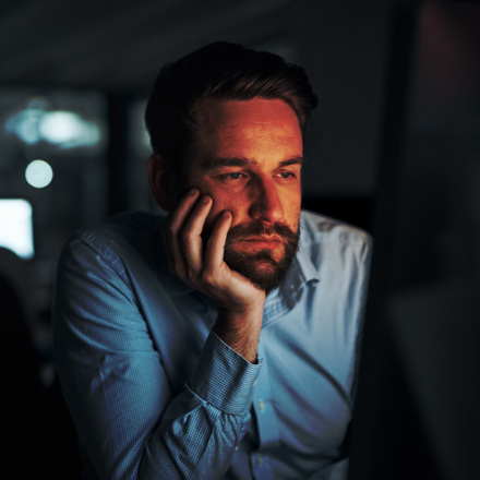 Shot of a young businessman looking tired while working on a computer in an office at night