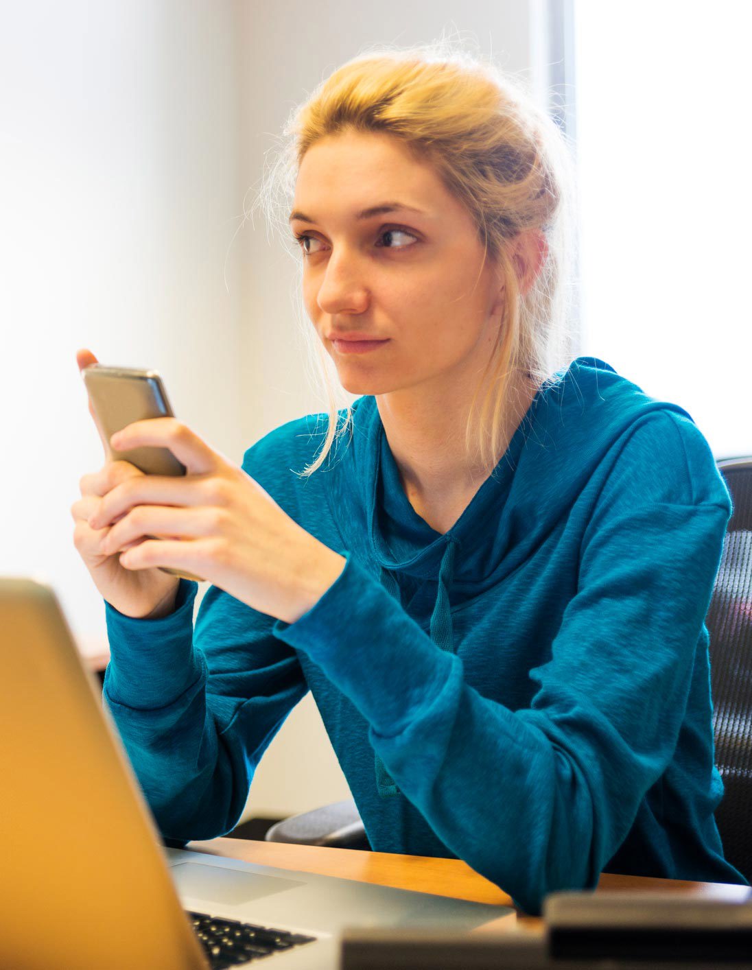 A young woman, Millennial, texting on her smart phone at work, not sure if it's allowed.