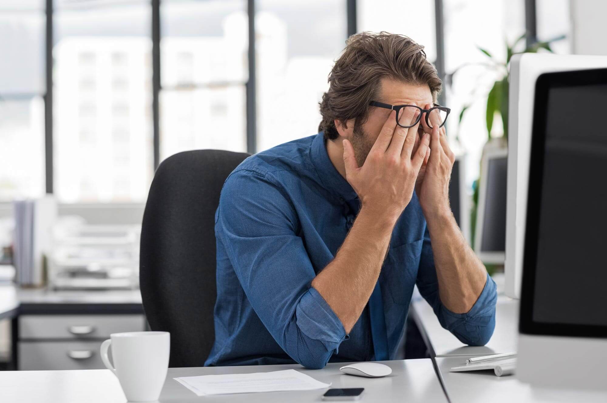 Portrait of an upset businessman at desk in office. Businessman being depressed by working in office. Young stressed business man feeling strain in eyes after working for long hours on computer.