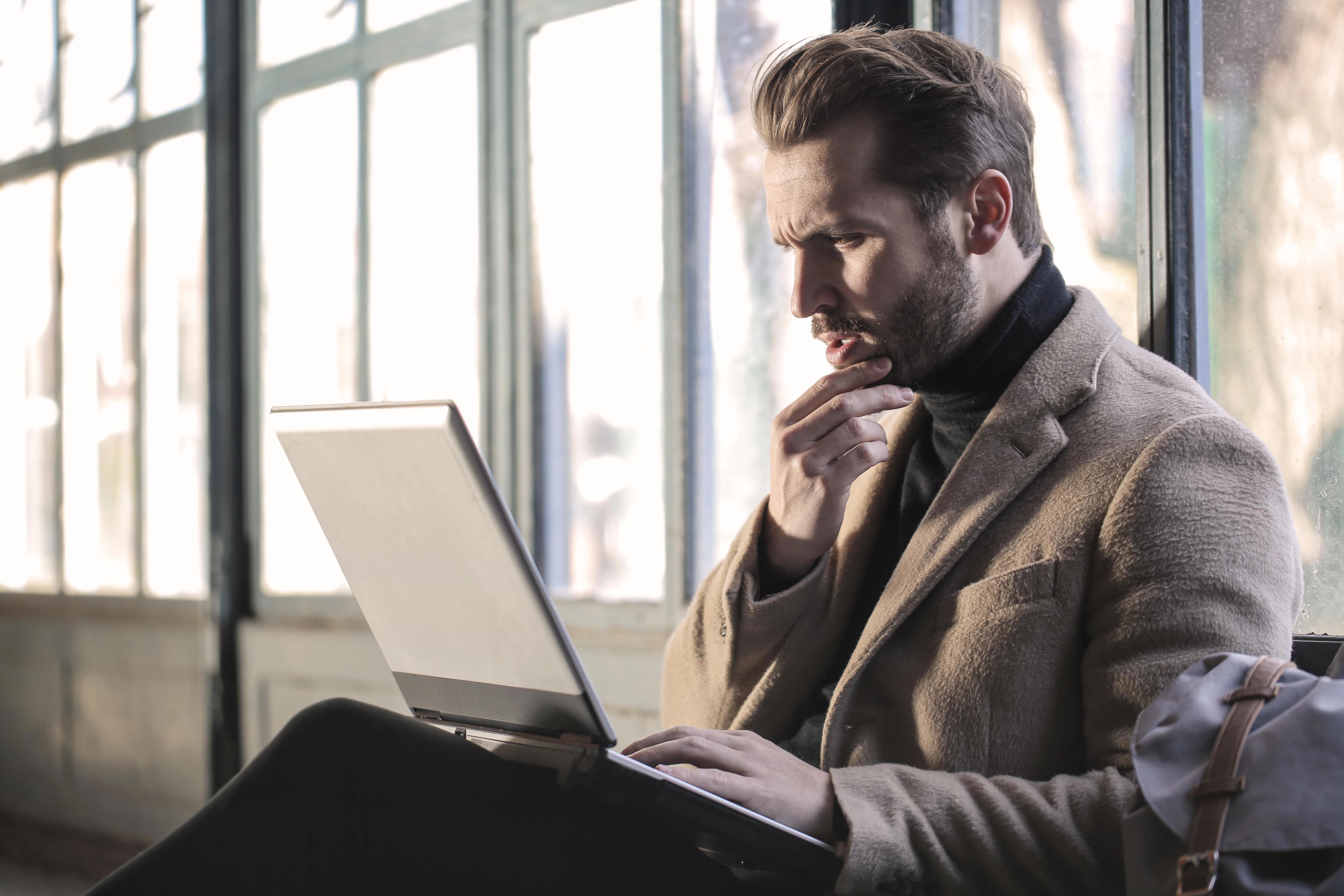 Man Wearing Brown Jacket And Using Grey Laptop