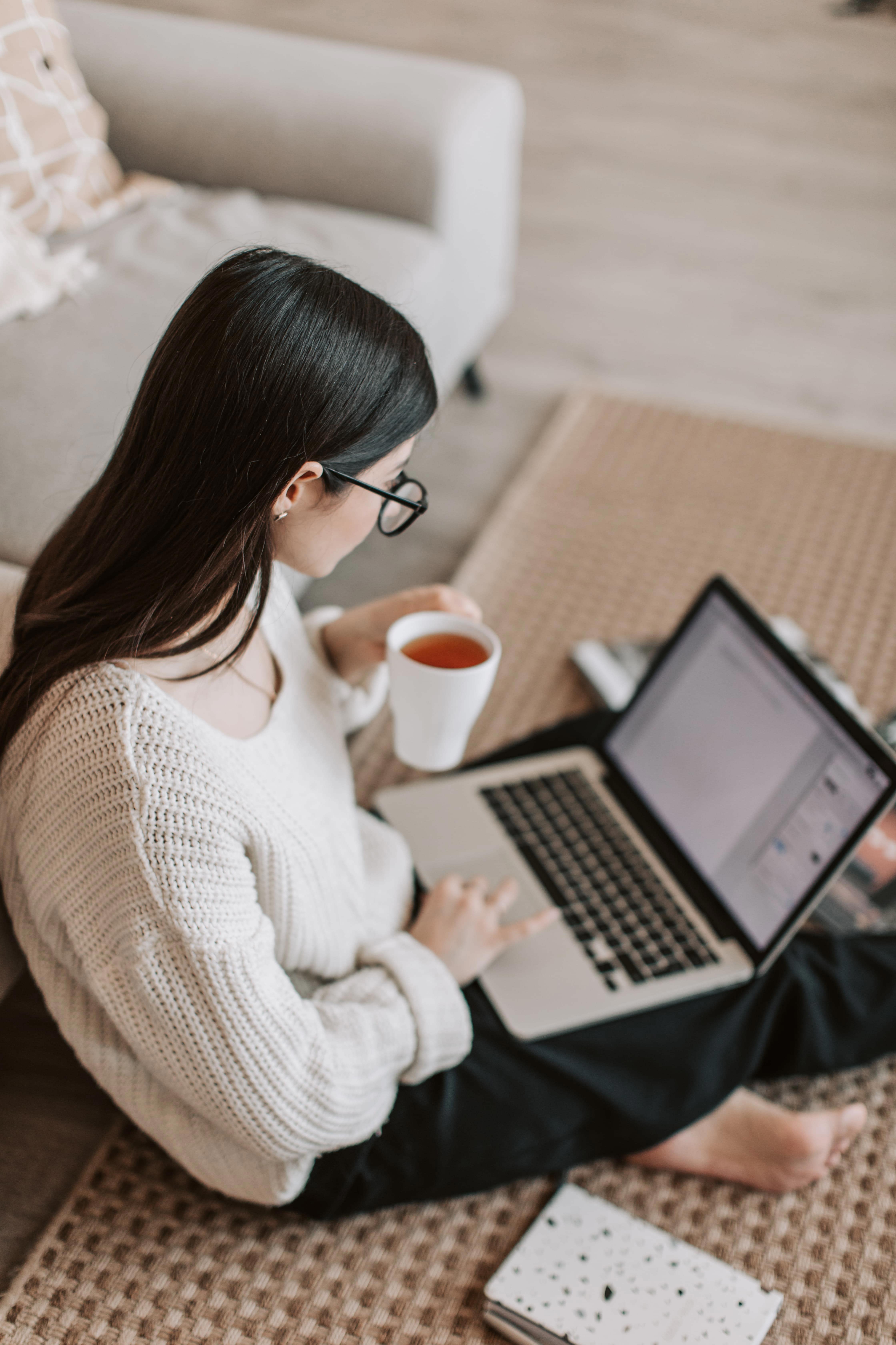 A woman sitting on the floor with a laptop and a cup of tea